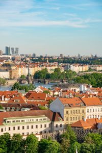A stunning aerial view of historic Prague with red rooftops and lush greenery under a clear blue sky.
